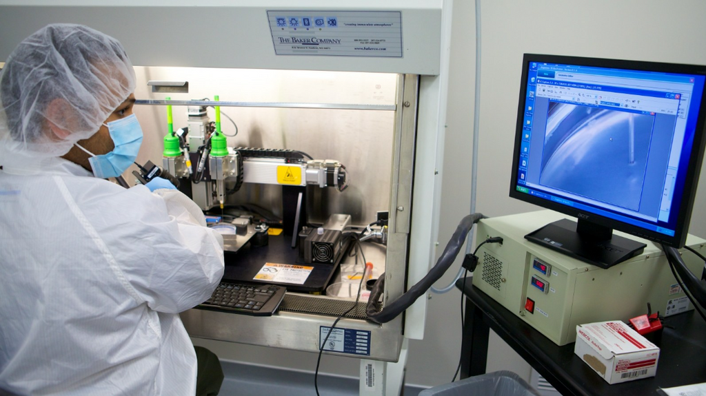 A lab worker in protective gear operating an AI-guided bioprinter to create living tissue structures inside a sterile hood.  