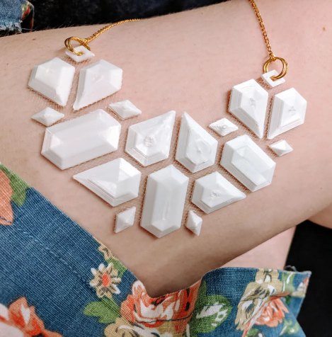 A 3D printed, geometric white statement necklace worn by a person.