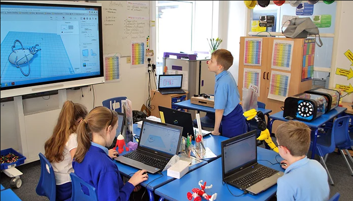 Students in a classroom using laptops and an interactive whiteboard to design 3D models alongside a desktop 3D printer.