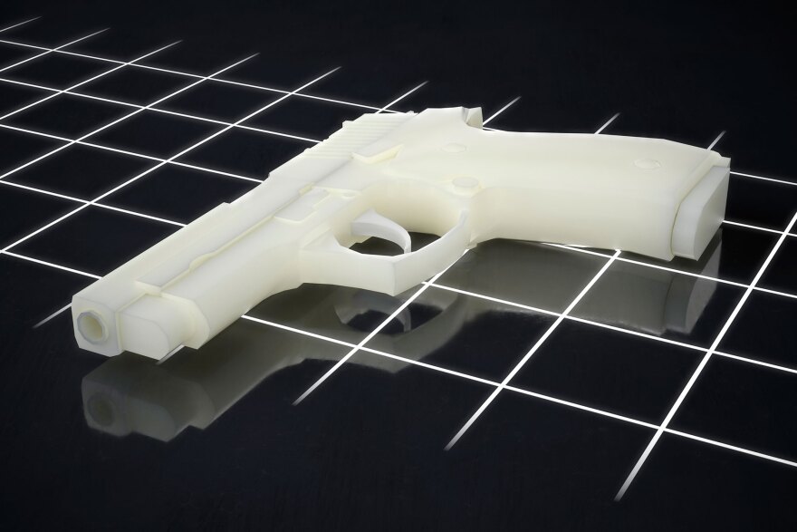 A white, 3D-printed plastic handgun—often referred to as a ghost gun—resting on a dark, grid-patterned surface