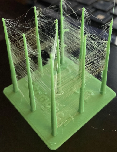 A green 3D print demonstrating severe stringing between thin vertical pillars.