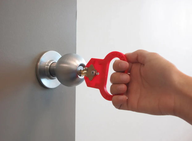 Hand turning a door lock using a red 3D-printed key turner aid.