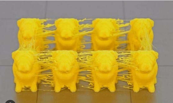 Multiple yellow 3D-printed dog figures exhibiting extreme stringing and oozing between the models.  