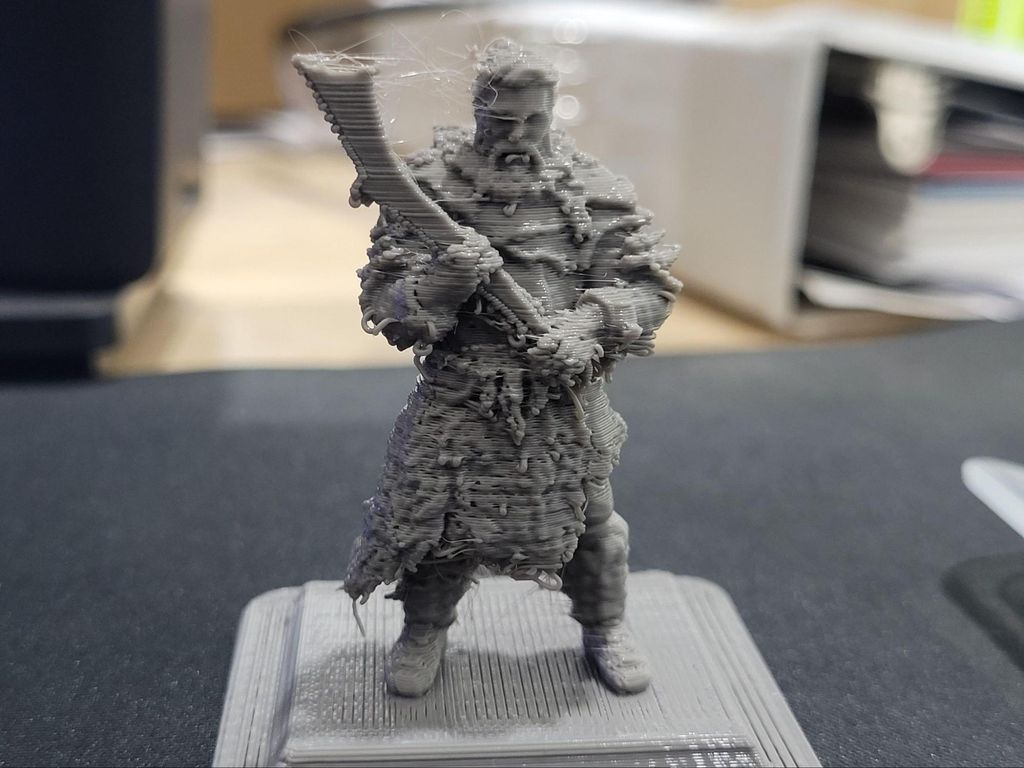 A 3D printed grey warrior figurine displaying severe stringing and a fuzzy surface texture