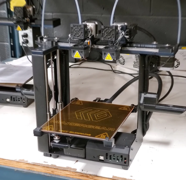 A MakerGear M3-ID professional dual-extruder desktop 3D printer set up on a workbench.  