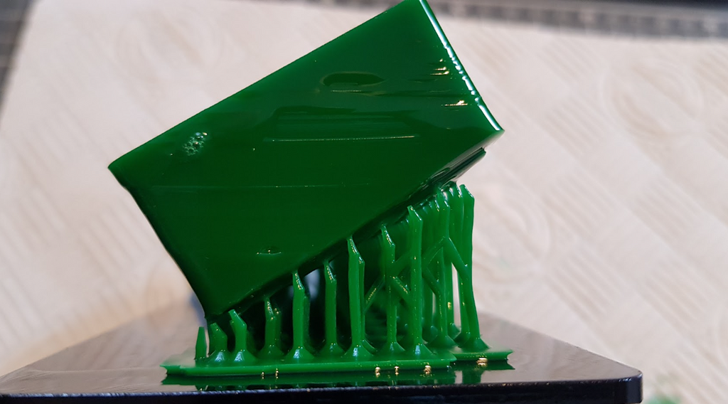Resin 3D printer with an orange UV cover showing a complex grey 3D printed model successfully attached to the build plate