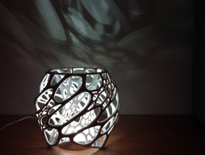 A glowing 3D printed cellular lamp with an organic, web-like structure casting dynamic shadows on the wall behind it