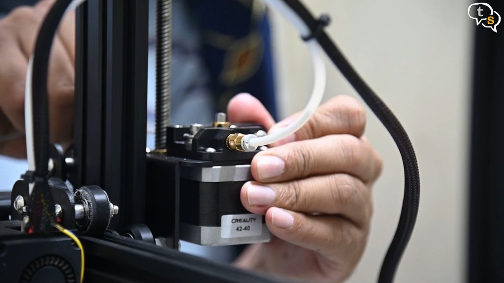 Close-up of a person's hands carefully feeding a new filament line into the extruder of a desktop 3D printer to perform a mid-print color change.