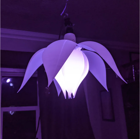 A hanging 3D printed flower lampshade illuminated with a purple light, featuring large, gracefully drooping posable petals