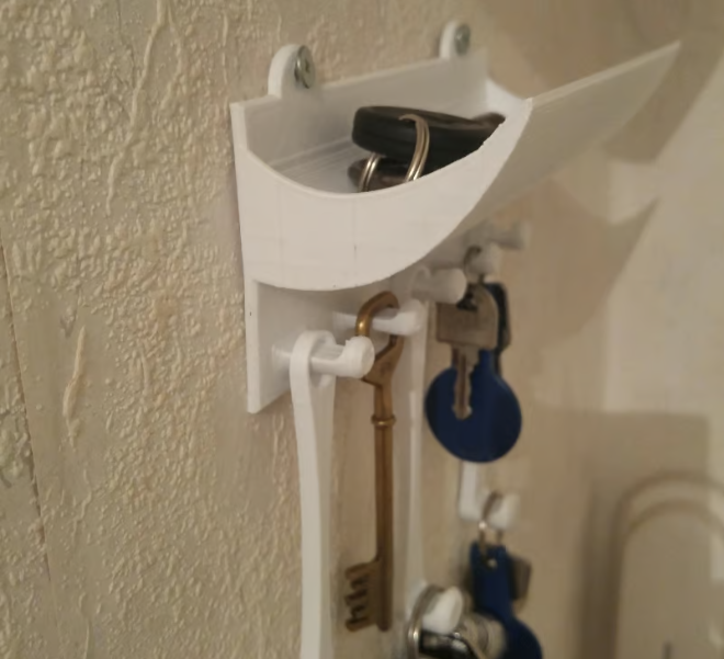 A white 3D-printed wall-mounted key organizer featuring a curved top shelf for loose items and several bottom hooks for hanging keys.