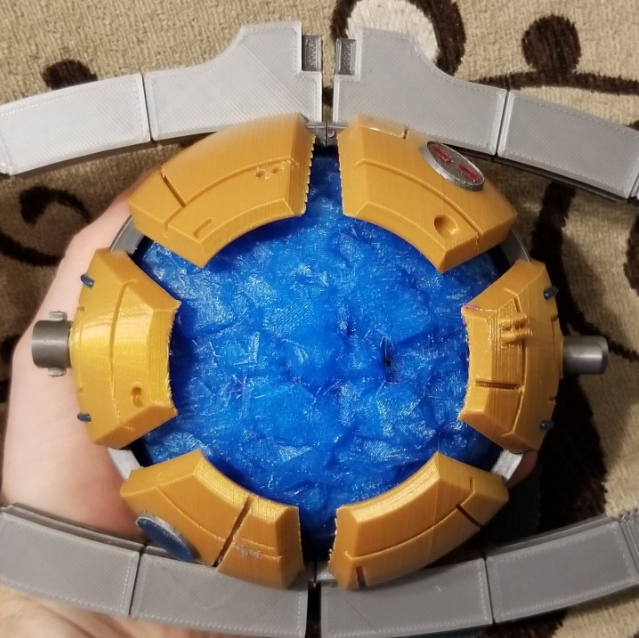 A highly detailed 3D printed Matrix of Leadership prop from Transformers, featuring a glowing blue center surrounded by a golden casing.