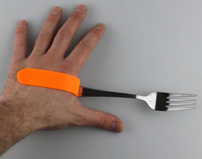 Hand wearing an orange 3D-printed adaptive grip attached to a metal fork.
