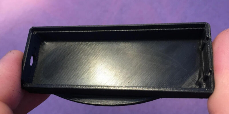 A close-up of a black 3D printed part demonstrating a flawlessly smooth top surface created using Cura ironing.
