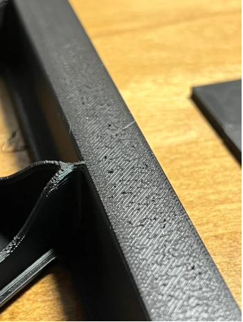 Close-up of a 3D printed black part displaying surface inconsistencies and tiny gaps due to incorrect ironing line spacing or poor filament flow.