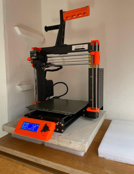A 3D printer resting on a heavy concrete paving stone layered over a thick white foam pad to dampen mechanical vibrations