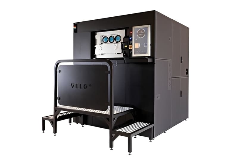 The Velo3D Sapphire metal 3D printer, a large black industrial system equipped with an attached step platform.  