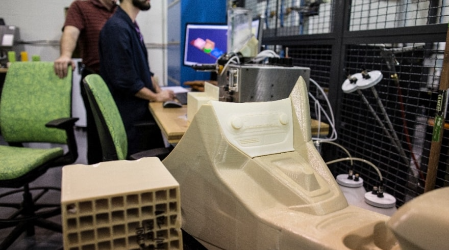 A rapid prototyping lab showing a 3D printed car dashboard component on a workbench.