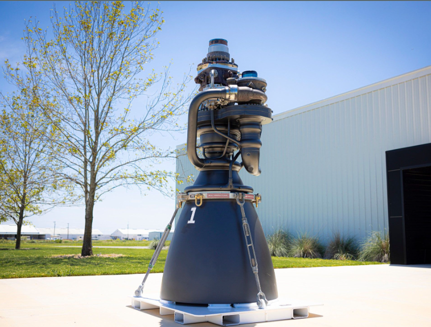 A full view of a SpaceX Raptor engine standing outdoors, featuring intricate plumbing and consolidated components achieved through advanced metal 3D printing.