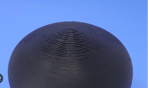 A close-up inspection of a 3D printed dome structure, revealing visible layer lines and uneven extrusion at the top peak.