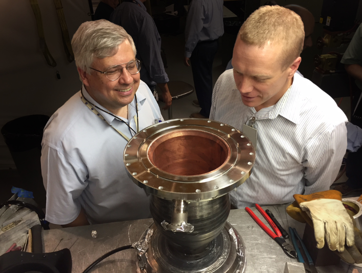 Two NASA researchers closely inspecting a shiny, newly manufactured 3D-printed rocket engine nozzle with a copper interior on a laboratory workbench.