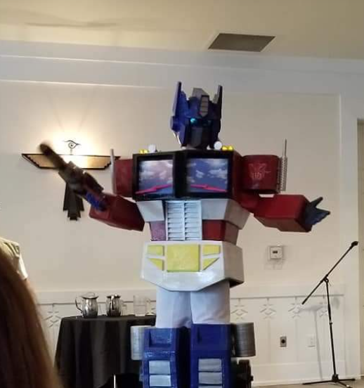 A person wearing a massive, full-sized 3D printed Optimus Prime cosplay costume standing indoors at an event.
