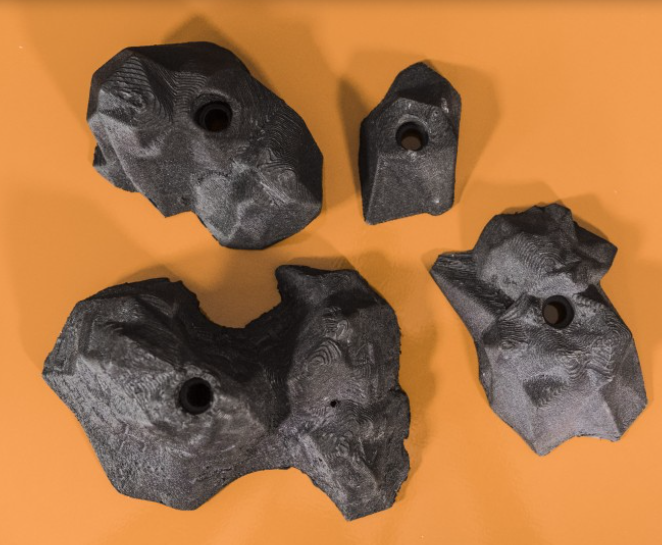 Four dark grey, highly textured, angular rock climbing holds resembling natural stone