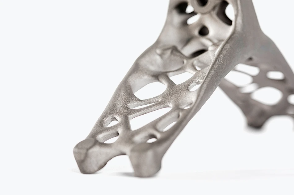 A topology-optimized 3D printed titanium part featuring complex, organic, web-like lattice structures designed to reduce weight while maintaining high strength.