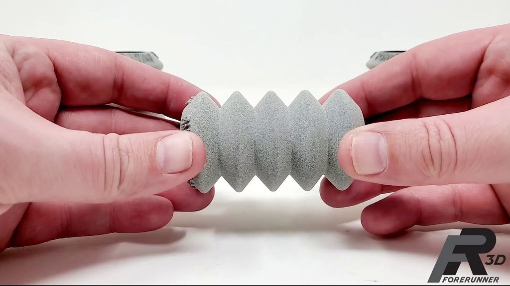 Two hands stretching a grey, flexible accordion-like 3D printed part to demonstrate TPU elasticity and strong first-layer adhesion